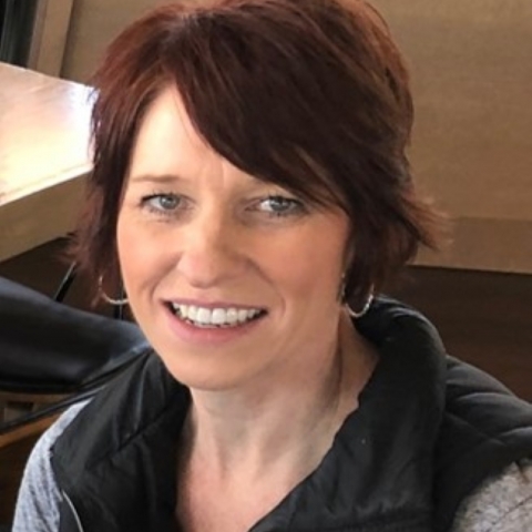 A portrait of a woman smiling from her shoulders up with short auburn hair
