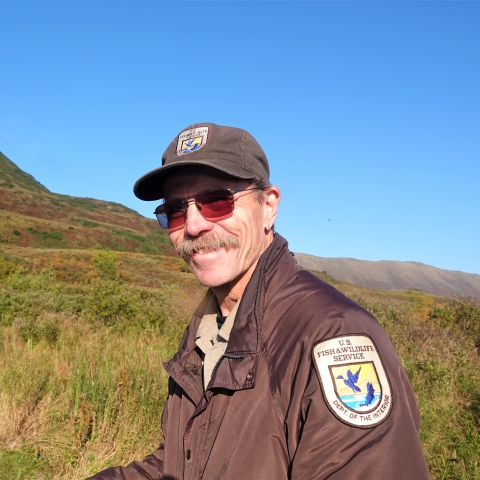 man in sunglasses and USFWS uniform with grassy hillside in the background
