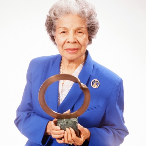 older lady in blue jacket holding plague with cooper circle and rock for base