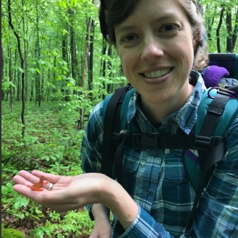 Clare smiles holding a small red salamander in a blue flannel