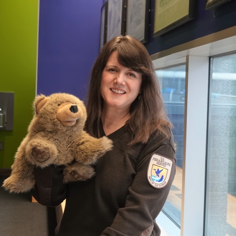 woman in USFWS sweater poses holding a brown bear puppet