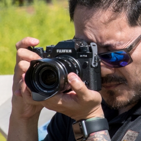 A guy with sunglasses looks through a camera lens