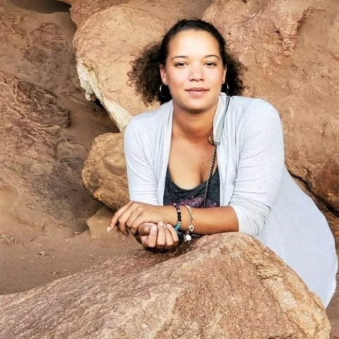 A smiling woman leaning on a sandstone-color rock