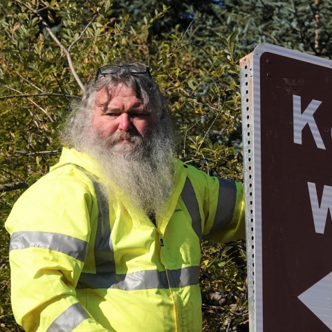 main in high visibility jacket standing next to a sign that reads Kodiak Wildlife