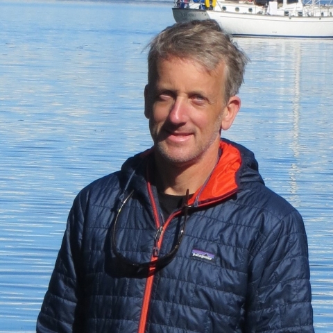 David Hand in a blue puffer jacket with a fishing boat in the background