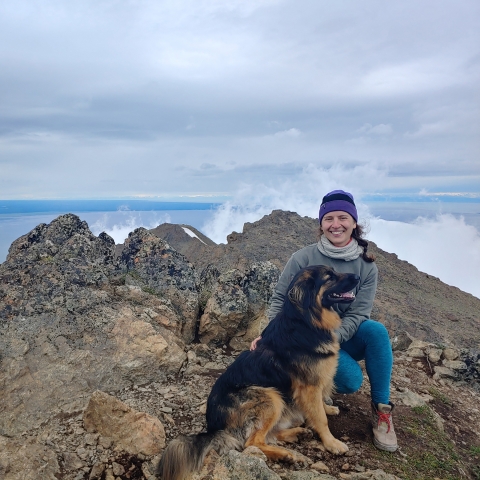 Woman in beanie with a dog on a mountain peak