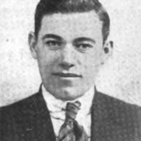 The photo is black and white headshot of a man in a suit and tie. 