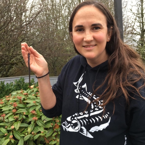 Julie Harris, Biometrician at CRFWCO, holding a juvenile Pacific Lamprey in the palm of her hand while wearing a black hoodie. Julie is standing next to bushes in a natural setting 