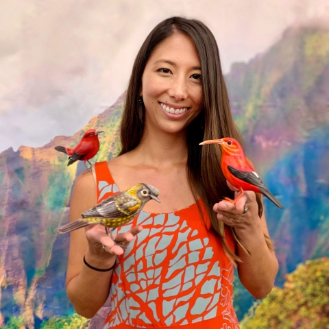 A woman wearing a red dress holds several native Hawaiian forest birds