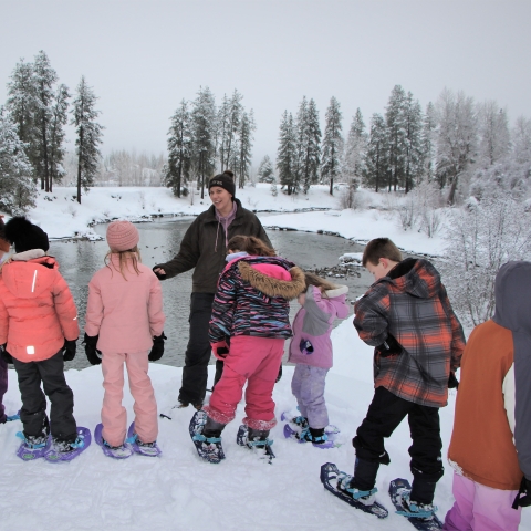 A FWS employee stands with a group of young students in snow gear with Icicle Creek and a snow covered landscape in the background