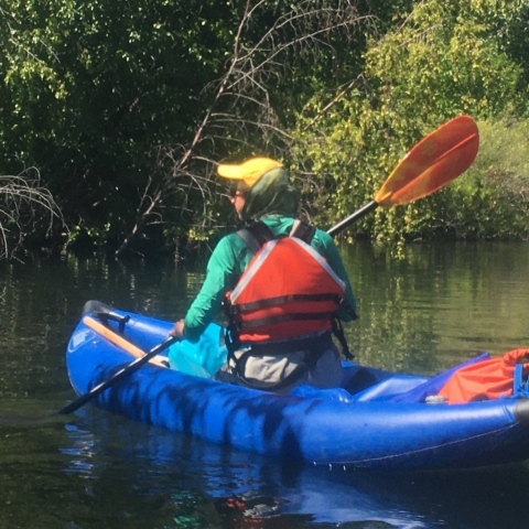 Woman in a PFD paddling an inflatable kayak