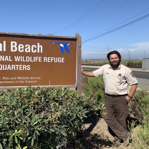 Refuge Manager for Seal Beach NWR stands next to refuge sign