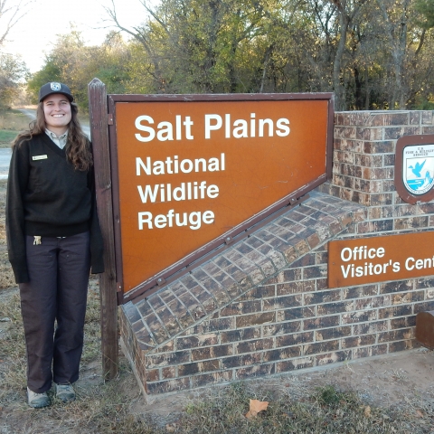Visitor Services Specialist Melissa Robell standing beside Salt Plains NWR Office/Visitor Center sign