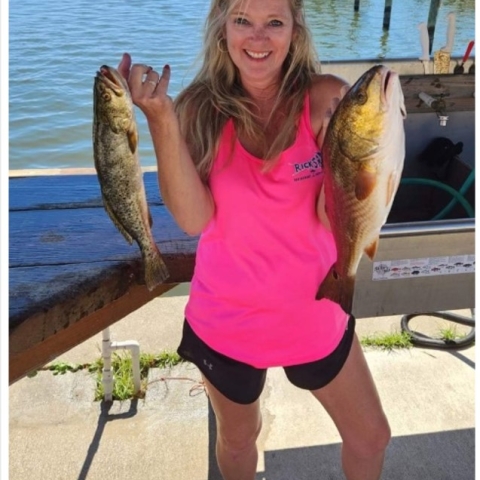 Michelle stands with two fish in a pink shirt and black short