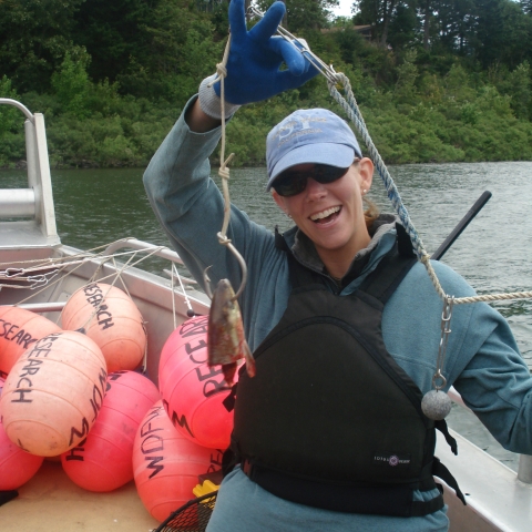 Molly stands on a boat smiling and holding a fish head on a hook