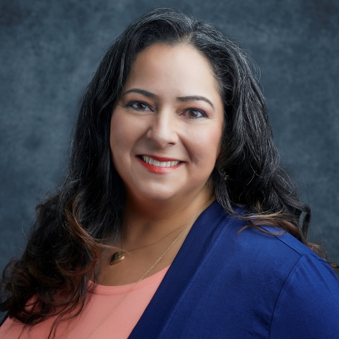 Woman smiles to the camera. She is wearing an orange and blue top.