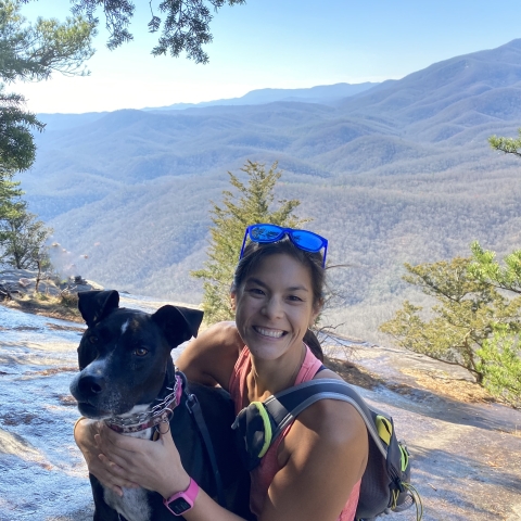 A picture of a woman with a dog on a sunny day with mountains in the background