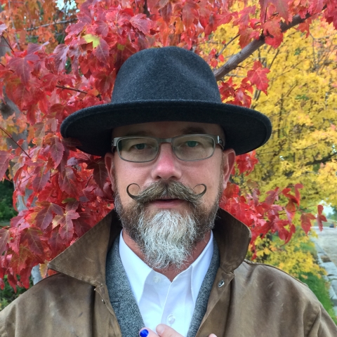 man in hat in front of fall leaves