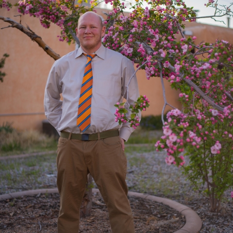 Man wearing a tie standing in front of tree with pink blossoms.