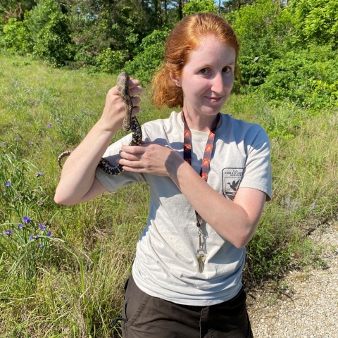 A biologist in USFWS uniform holding a snake in the field
