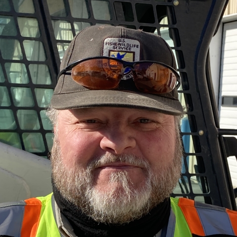 man in safety vest and hat sits in a grader