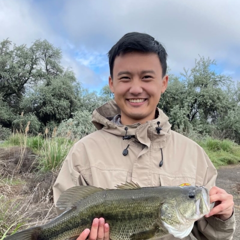 Ywj Pheej Yang holding a largemouth base with a natural setting in the background