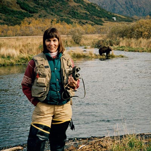woman standing by stream wearing wading boots and holding binoculars