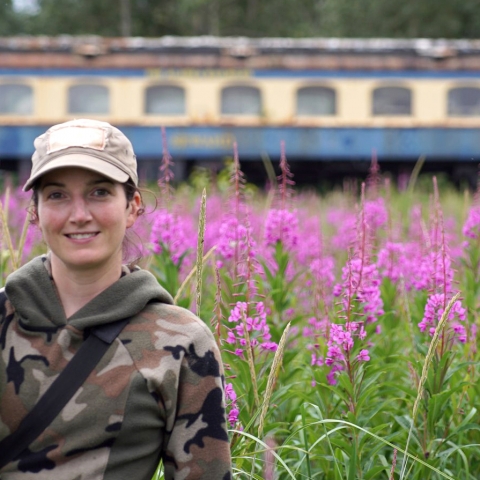 woman standing by fireweed and an old train