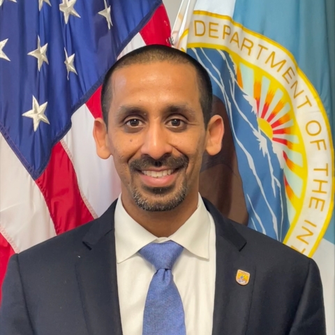portrait photo of Mr. Sundaresan standing in front of the U.S. and Department of Interior flags
