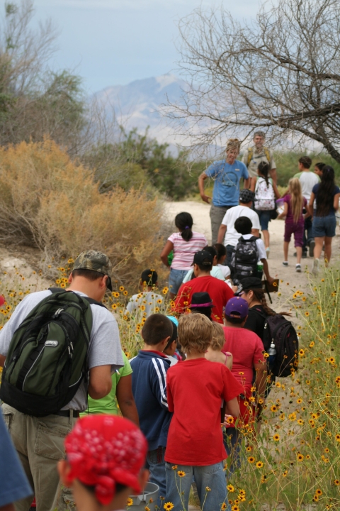 Kids and adults walk along a trail between brush at Peterson Reservoir for a day of reptile exploration