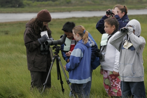 A Fish and Wildlife employee assists schoolchildren with using scopes and binoculars to view birds