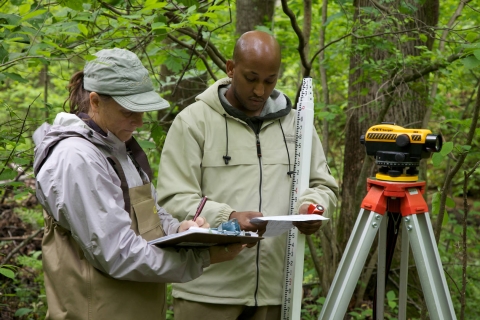 2 FWS employees holding clip boards writing what is being surveying and assessing rivers and streams