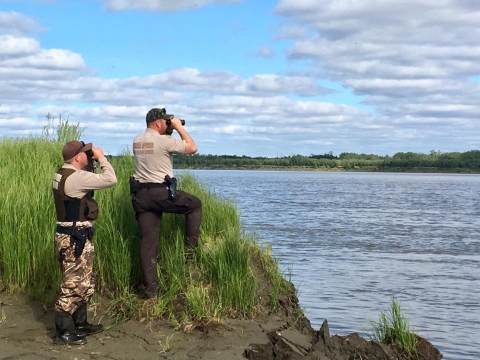 Two law enforcement officers using binoculars on a shoreline