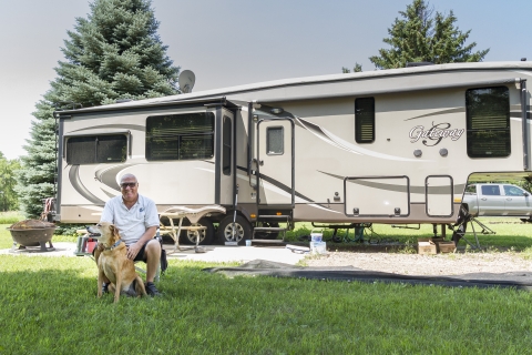 A retiree volunteer and his dog sit in front of their camper set up on the grounds of Gavins Point NFH