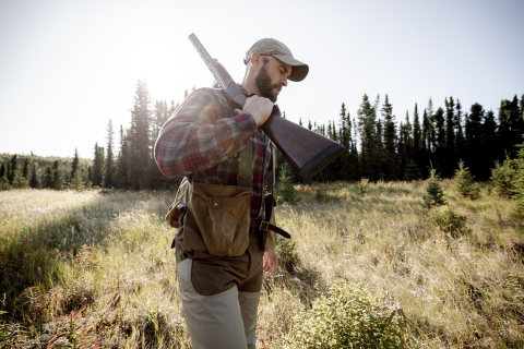 A man walking on a sunny day with a shotgun over his shoulder