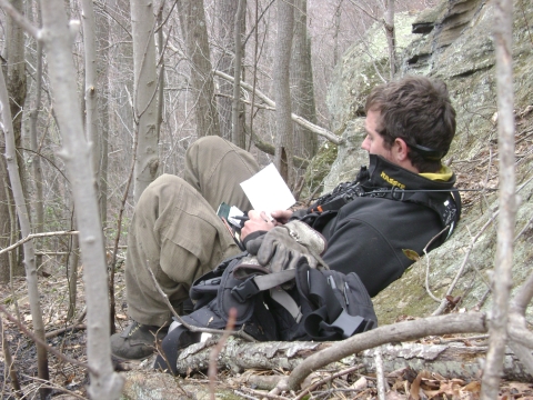 Intern sitting on rock with notebook and radio at Big Oaks NWR
