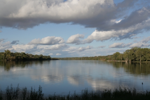 View of DeSoto Lake with trees on both sides and puffy clouds in sky reflected on water