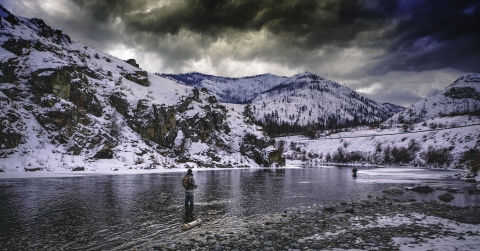 Anglers fish for steelhead in a river valley between mountains under a gray winter skies. 