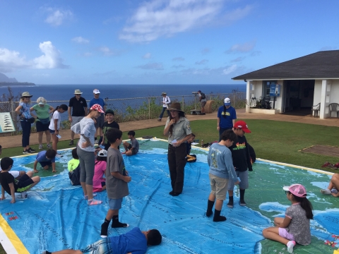 A group of elementary school kids explore a giant map of the pacific ocean that is on the ground