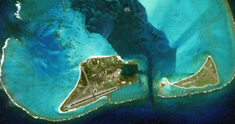 An aerial photograph of two small islands surrounded by bright turquiose water. The atoll is the result of a sunken volcano.