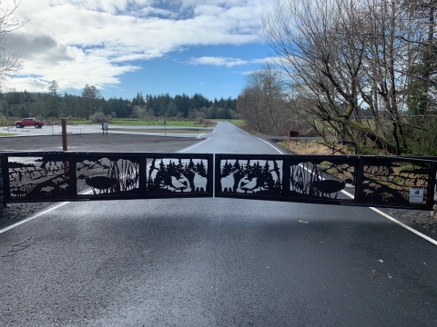 An iron gate with intricate designs of elk and birds across a road surrounded by trees