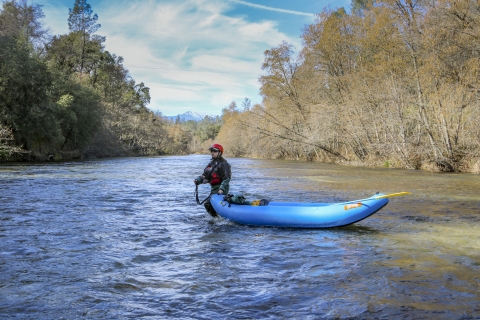 a woman walking in a river pulling a kayak with a mountain in the background.