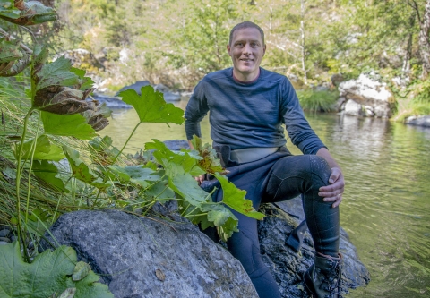 a man sitting on a rock next to a river posing for the camera