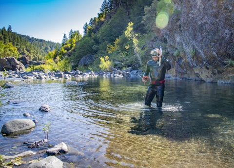photo of a man in a wetsuit standing in a stream