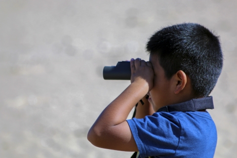 A young boy looks through a pair of binoculars