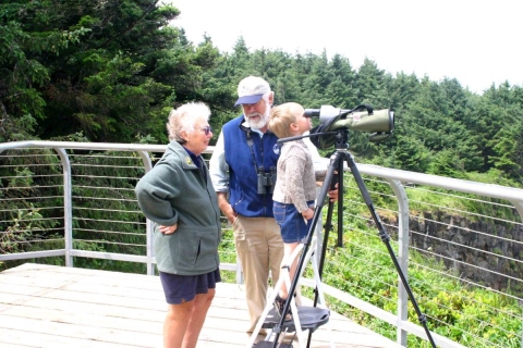A volunteer speaks with a woman as he assists a young boy in observing wildlife through a spotting scope