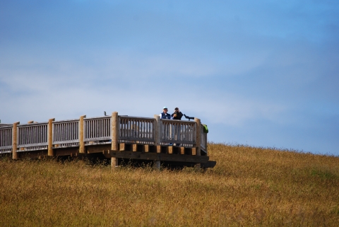 A wooden observation platform atop a browning-grass hilltop amid a blue sky