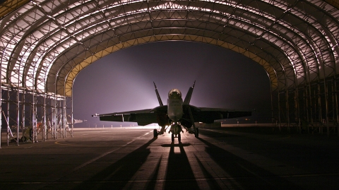 silhouette of a fighter jet sitting under a sun shade