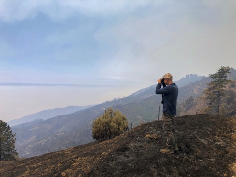 A man looks out over a smoky mountain using binoculars