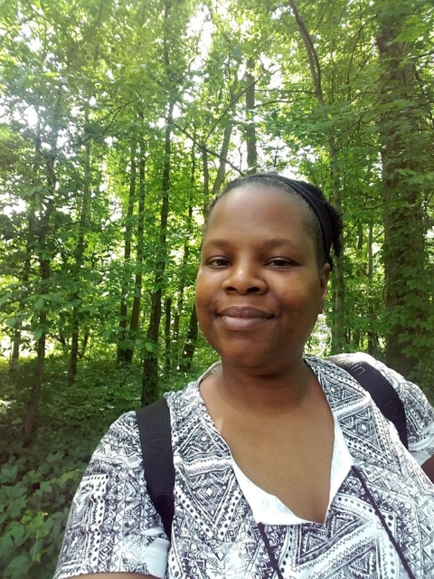 A smiling woman stands in woods.